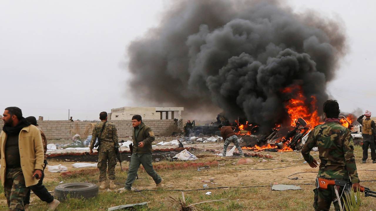 Xiitas caminham com suas armas perto de um veículo que explodiu durante um ataque na zona sul de Tikrit (Iraque) - 12/03/2015