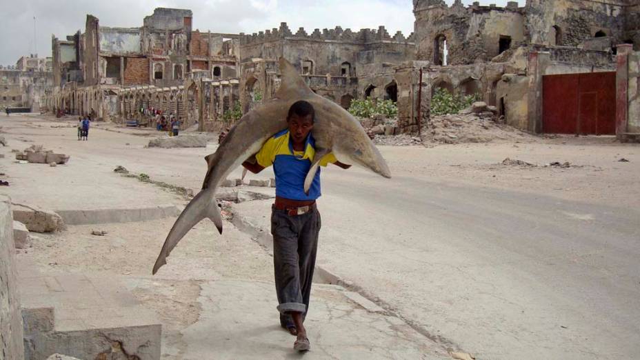 Homem carrega tubarão pelas rua de Mogadishu, Somália