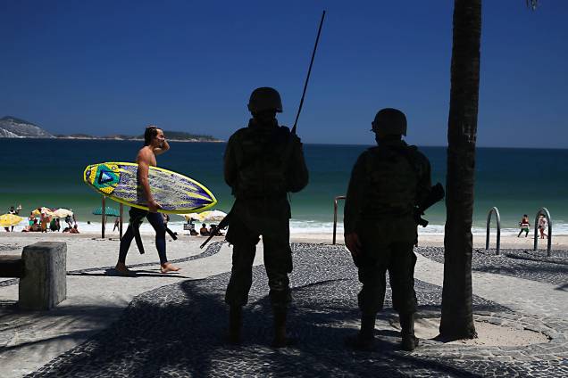 Surfista passa por soldados do exército que fazem a segurança na praia do Arpoador, RJ - 15/02/2017 Surfista passa por soldados do exército que fazem a segurança na praia do Arpoador, RJ - 15/02/2017