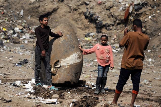 Crianças fazem fotos próximas a cabeça de uma estátua do faraó Ramsés II encontrada por trabalhadores em uma favela no Cairo - 09/03/2017 Crianças fazem fotos próximas a cabeça de uma estátua do faraó Ramsés II encontrada por trabalhadores em uma favela no Cairo - 09/03/2017