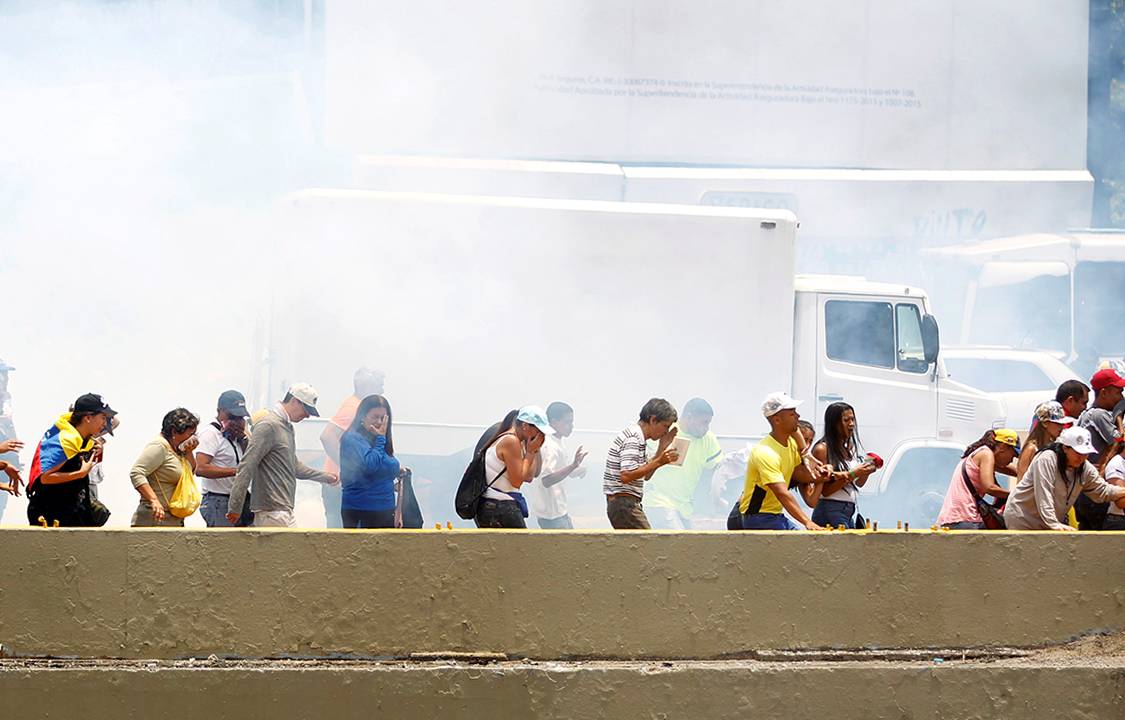 Manifestantes se protegem das bombas de gás lacrimgêneo lançadas pela polícia durante protesto contra o presidente Nicolás Madura, em Caracas, na Venezuela