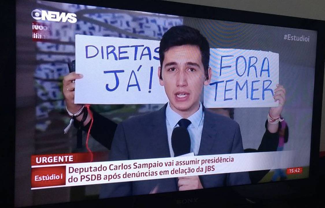 Manifestante segura cartaz em reportagem da Globo News