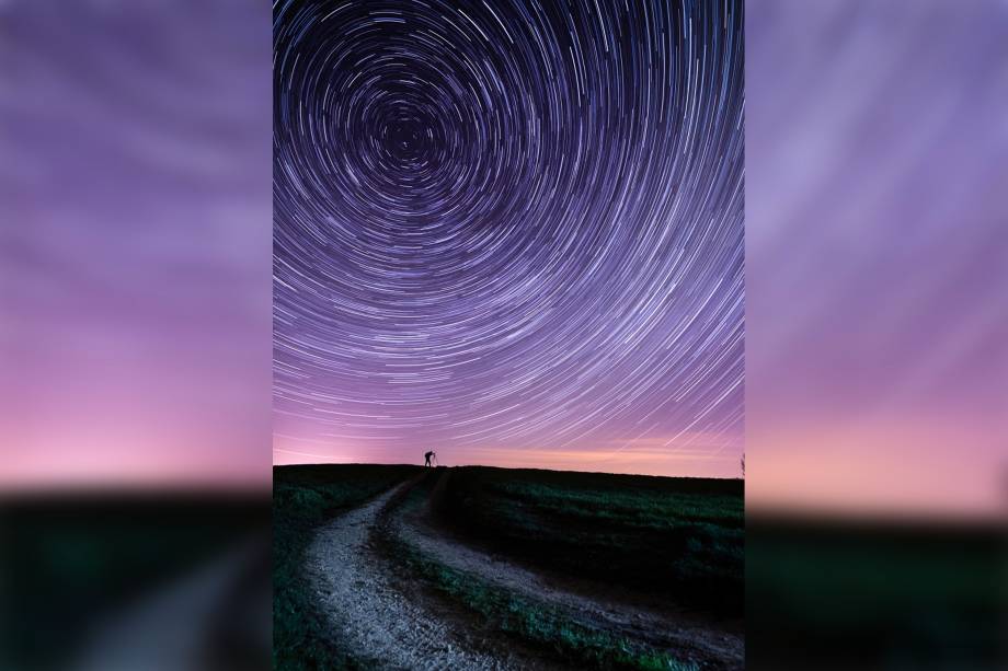 <span>Faixas radiante e concêntricas de uma estrela aparentemente giram sobre um observador solitário contra o roxo e rosa brilhante do céu noturno. A foto foi tirada durante a hora em que os relógios "avançavam" para começar o horário de verão britânico.</span>