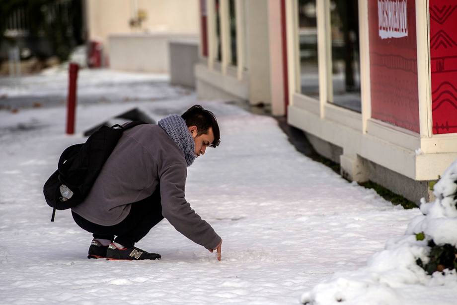 Pessoa se distrai com camada de neve no chão, após forte nevasca atingir a região de Santiago, no Chile - 15/07/2017