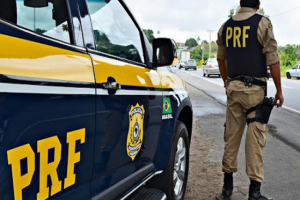 .Agente da PRF observa a rodovia ao lado de sua viatura