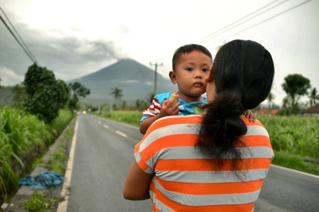 Mulher carrega seu bebê em estrada com vista para o vulcão Agung, em Bali, na Indonésia Mulher carrega seu bebê em estrada com vista para o vulcão Agung, em Bali, na Indonésia
