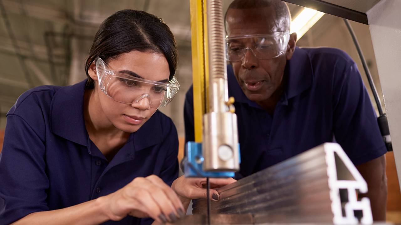 Carpinteiro ensina mulher a utilizar máquina em linha de produção