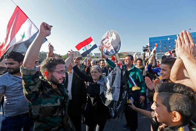 Manifestantes sírios agitam bandeiras e seguram retratos do presidente Bashar al-Assad, enquanto se reúnem na Praça Umayyad, em Damasco, para reivindicar o bombardeio realizado pelos Estados Unidos, Reino Unido e França - 14/04/2018 Manifestantes sírios agitam bandeiras e seguram retratos do presidente Bashar al-Assad, enquanto se reúnem na Praça Umayyad, em Damasco, para reivindicar o bombardeio realizado pelos Estados Unidos, Reino Unido e França - 14/04/2018