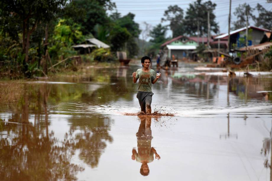 Homem atravessa uma estrada inundada em uma aldeia em Sanamxai, na província de Attapeu, no Laos - 26/07/2018