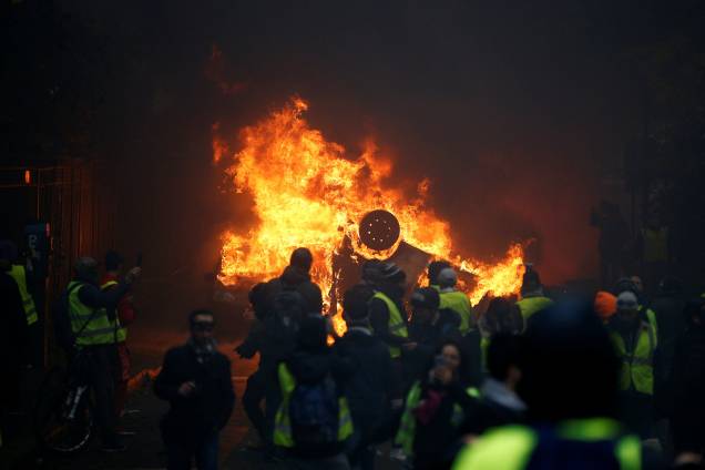 Manifestantes de colete amarelo são vistos próximos a um carro em chamas durante protesto na Place de l'Etoile em Paris, França - 01/12/2018 Manifestantes de colete amarelo são vistos próximos a um carro em chamas durante protesto na Place de l'Etoile em Paris, França - 01/12/2018