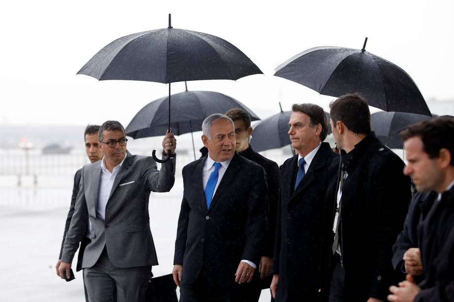 A comitiva do primeiro-ministro israelense, Benjamin Netanyahu, segura guarda-chuvas enquanto caminham com o presidente brasileiro Jair Bolsonaro durante uma cerimônia de boas-vindas em sua chegada à Israel - 31/03/2019