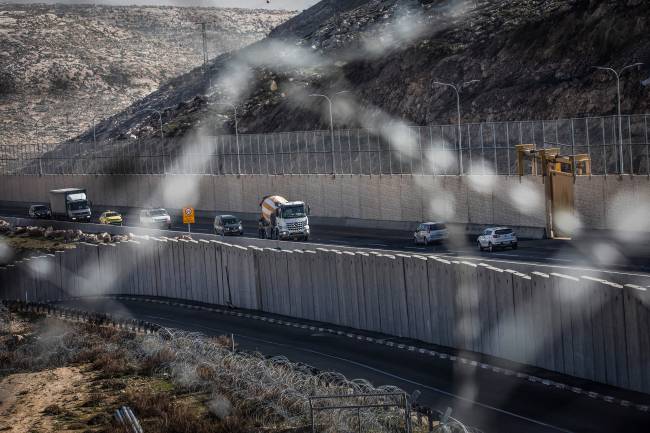 Veículos trafegam na polêmica rodovia da Cisjordânia, dividida por um grande muro de concreto segregando o tráfego israelense e palestino