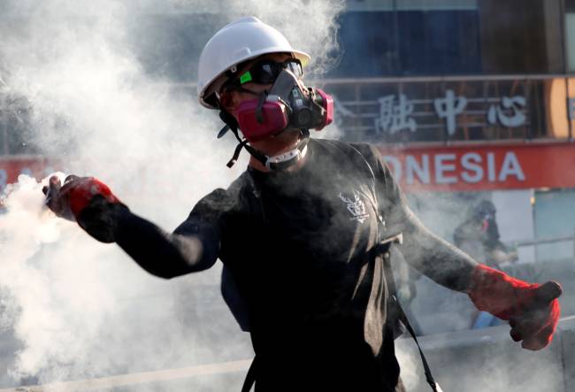 A protester throws a tear gas canister back at the police during a demonstration in support of the city-wide strike and to call for democratic reforms in Hong Kong
