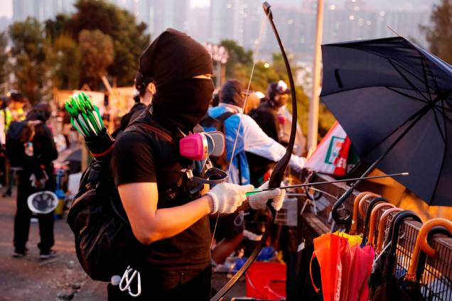 Um manifestante antigoverno utiliza um arco e flecha improvisado durante um impasse com a polícia de choque na Universidade Chinesa de Hong Kong, em Hong Kong, na China Um manifestante antigoverno utiliza um arco e flecha improvisado durante um impasse com a polícia de choque na Universidade Chinesa de Hong Kong, em Hong Kong, na China