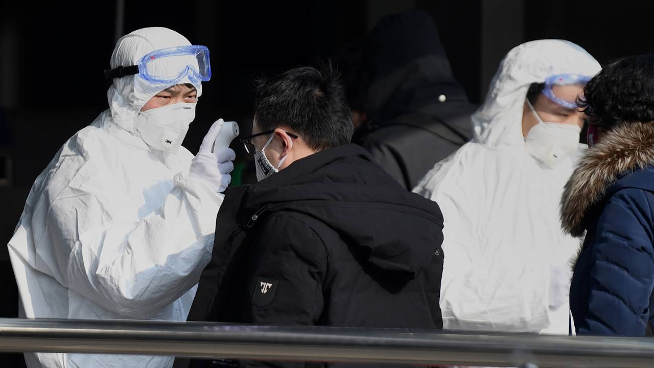Viajantes são verificados pelos agentes de segurança que usam roupas especiais na entrada da estação de trem em Pequim, na China