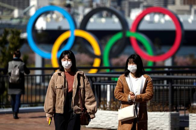 People wearing protective face masks are seen in front of the Giant Olympic rings at the waterfront area at Odaiba Marine Park in Tokyo