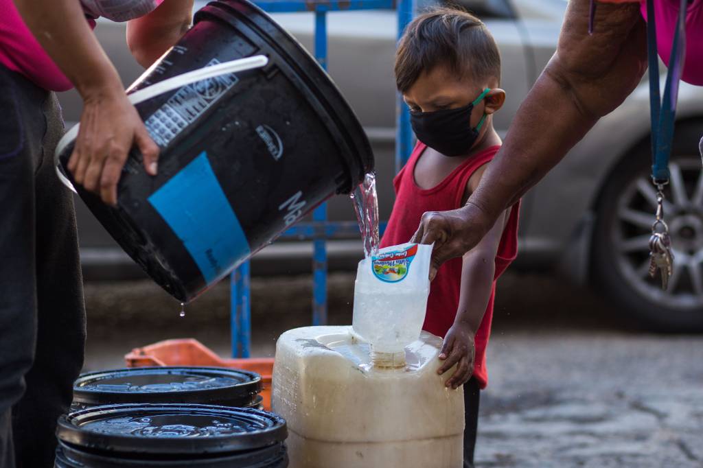 VENEZUELA-HEALTH-VIRUS-GASOLINE-WATER Criança com máscara observa coleta de água em recipientes precários em Caracas: crise humanitária e festas nababescas -27/03/2020