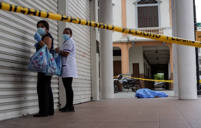 Women stand near the dead body of a man who had collapsed on the sidewalk, during the outbreak of coronavirus disease (COVID-19), in Guayaquil Women stand near the dead body of a man who had collapsed on the sidewalk, during the outbreak of coronavirus disease (COVID-19), in Guayaquil