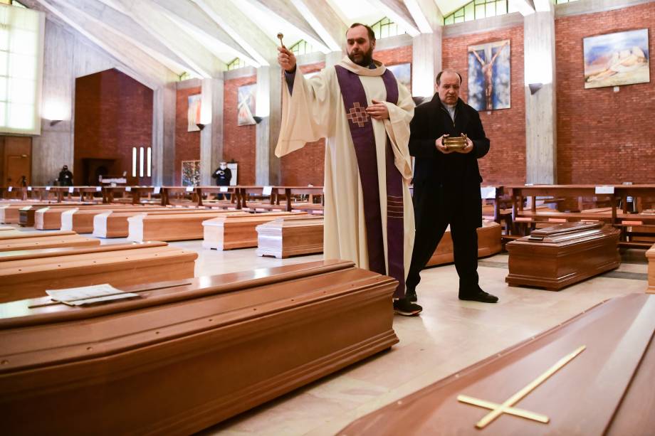 Bênção final: O padre Don Marcello asperge água benta sobre os esquifes de vítimas do coronavírus abrigados na igreja de San Giuseppe, em Seriate, na Itália