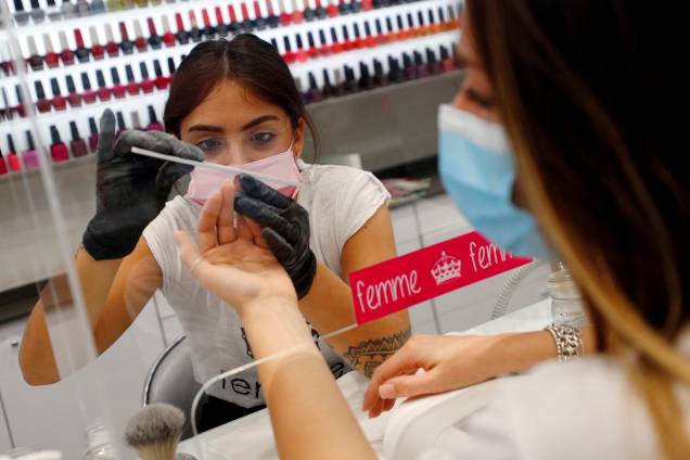 Manicure faz as unhas de cliente através de vidro protetor em Roma, Itália - 18/05/2020 Manicure faz as unhas de cliente através de vidro protetor em Roma, Itália - 18/05/2020