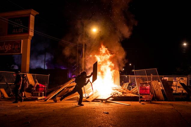 Um manifestante lança um pedaço de madeira em um incêndio na rua ao norte da 3ª Delegacia de Polícia em Minneapolis, Minnesota Um manifestante lança um pedaço de madeira em um incêndio na rua ao norte da 3ª Delegacia de Polícia em Minneapolis, Minnesota