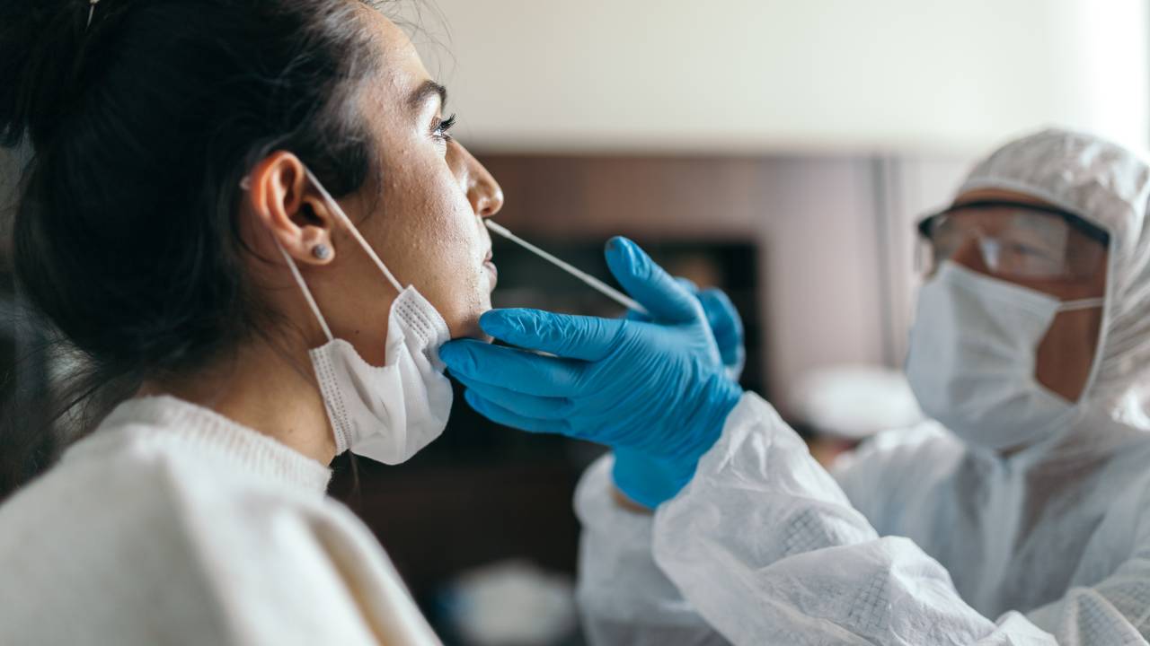 Doctor in protective workwear taking nose swab test from young woman