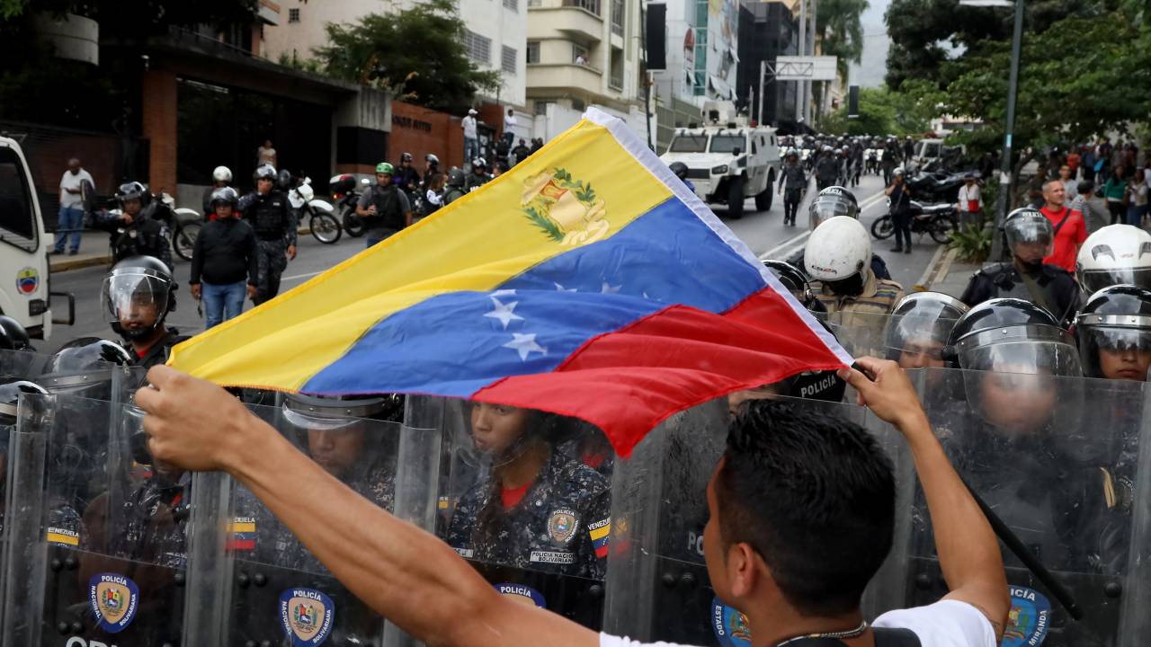 Manifestante segura bandeira da Venezuela ao lado de membros da tropa de choque da Polícia Nacional, em Caracas. 10/03/2020