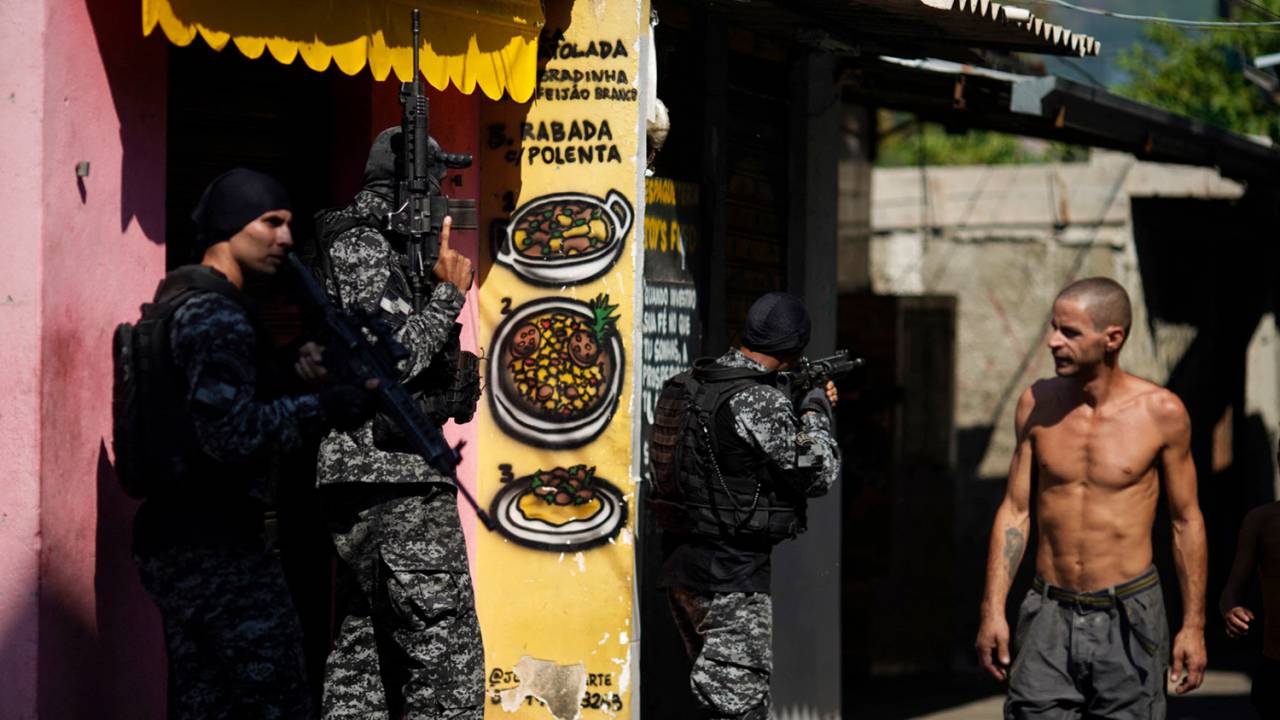 A local resident looks at Rio's Civil Police officers taking position during a police operation against drug traffickers at the Jacarezinho favela in Rio de Janeiro state, Brazil, on May 06, 2021. - A civil police officer and 22 suspects were killed during a police operation against drug traffickers in the Jacarezinho favela, Rio de janeiro on April 2021. The incident began with an exchange of fire at a metro station in the area which is in the North Zone of Rio de Janeiro. (Photo by MAURO PIMENTEL / AFP)