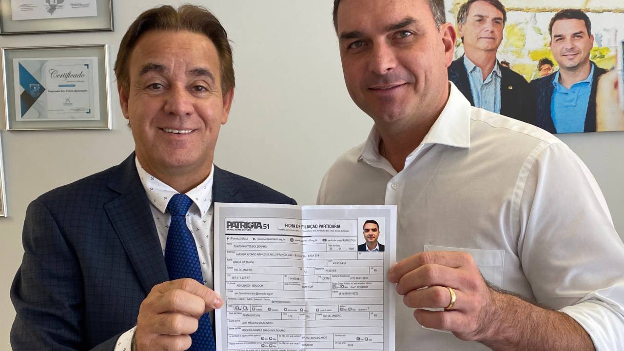 O presidente do Patriota, Adilson Barroso, e Flávio Bolsonaro exibem ficha de filiação do senador ao partido