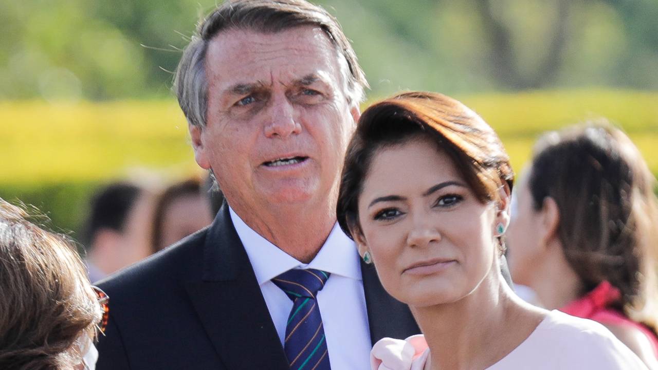 Brazilian President Jair Bolsonaro (L) participates in the flag-raising ceremony accompanied by his wife Michelle Bolsonaro on International Women's Day in front of the Alvorada Palace in Brasilia, on March 8, 2022. (Photo by Sergio Lima / AFP)
