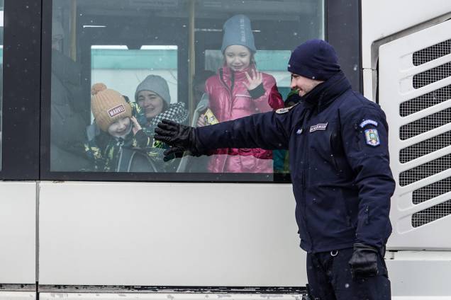 Um oficial da Gendarmaria romena sorri para refugiados ucranianos em um ônibus na fronteira romeno-ucraniana, em Siret - Um oficial da Gendarmaria romena sorri para refugiados ucranianos em um ônibus na fronteira romeno-ucraniana, em Siret -