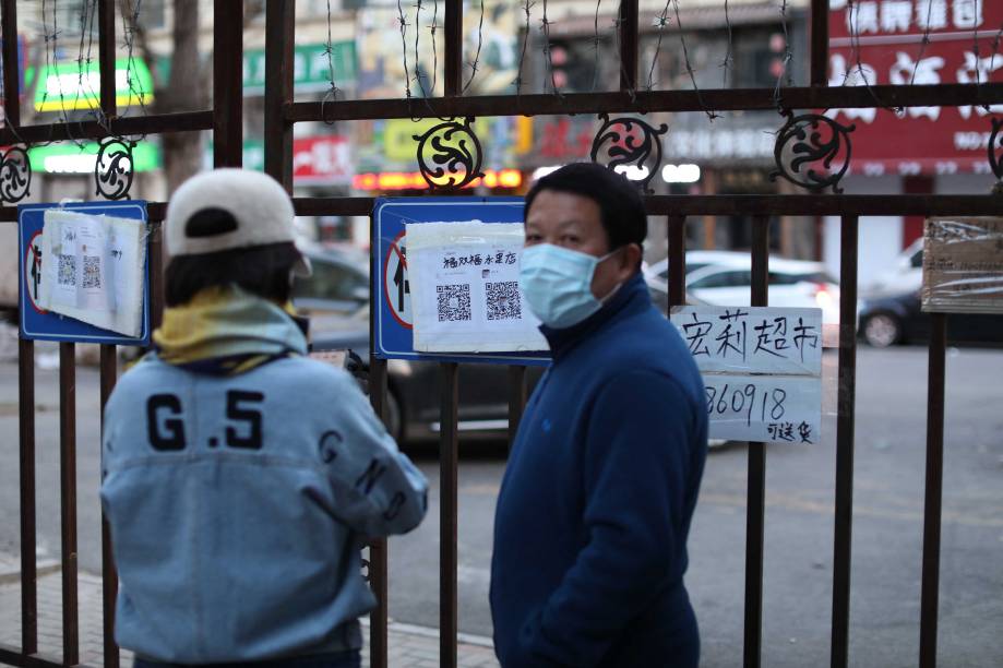 Moradores lendo quadros com números de telefone de lojas que podem entregar comida na entrada de uma área residencial restrita devido à disseminação do coronavírus, em Shenyang -