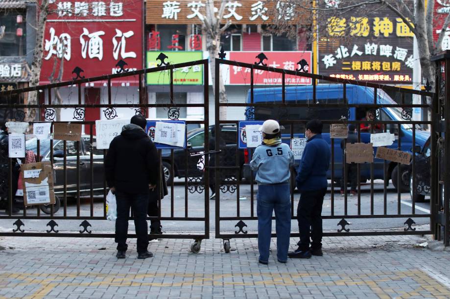 Moradores lendo quadros com números de telefone de lojas que podem entregar comida na entrada de uma área residencial restrita devido à disseminação do coronavírus, em Shenyang -