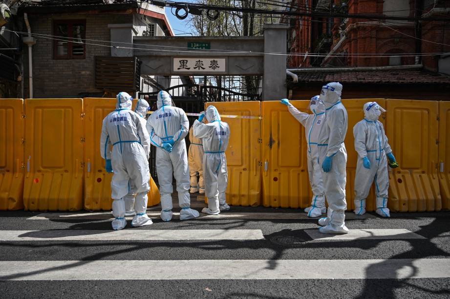 Trabalhadores do serviço público, que usam equipamentos de proteção, entregam vegetais`a moradores de um bairro confinado, no distrito de Jing'an, em Xangai.