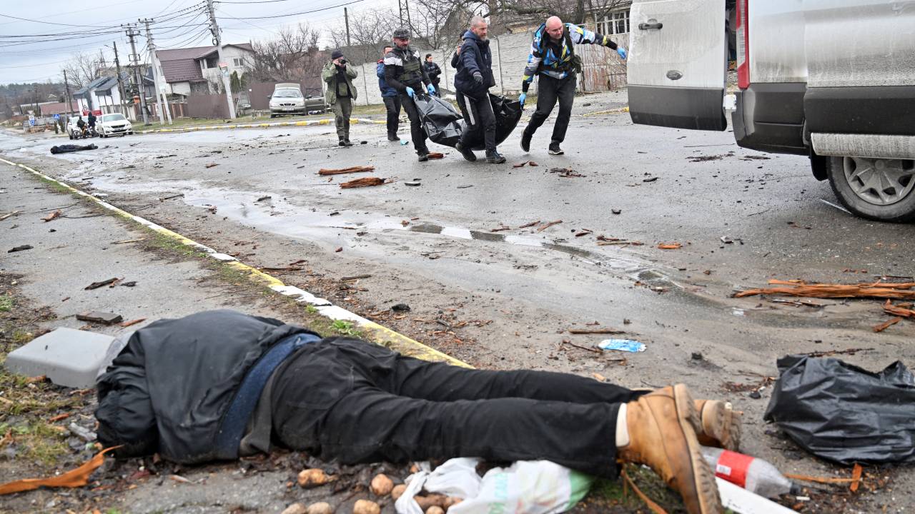 EDITORS NOTE: Graphic content / CAPTION ADDITION - Communal workers carry a civilian in a body bag as another corpse is seen on the ground in the town of Bucha, not far from the Ukrainian capital of Kyiv on April 3, 2022. US and NATO leaders voiced shock and horror at new evidence of atrocities against civilians in Ukraine, and warned that Russian troop movements away from Kyiv did not signal a withdrawal or end to the violence. - The Kremlin on April 4, 2022 rejected accusations that Russian forces were responsible for killing civilians near Kyiv. "We categorically reject all allegations," Kremlin spokesman Dmitry Peskov told journalists. (Photo by Sergei SUPINSKY / AFP)