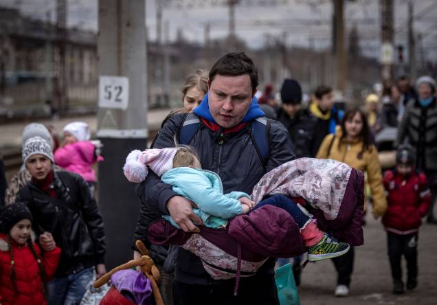 Um homem carrega uma menina ao chegar com outras famílias para embarcar em um trem na estação central de Kramatorsk - Um homem carrega uma menina ao chegar com outras famílias para embarcar em um trem na estação central de Kramatorsk -