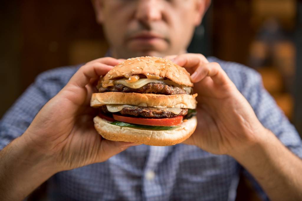 Man holding a big hamburger GORDUROSO - Apetite: a má alimentação aumentou os índices da doença -