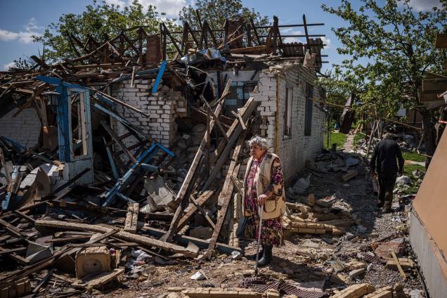 Um casal traz sua bagagem para fora de sua casa destruída na vila de Vilkhivka, perto da cidade oriental de Kharkiv, em 14 de maio de 2022. Um casal traz sua bagagem para fora de sua casa destruída na vila de Vilkhivka, perto da cidade oriental de Kharkiv, em 14 de maio de 2022.