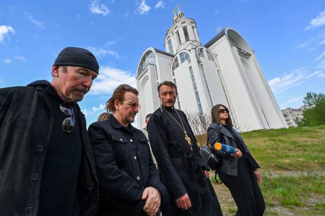 Andrii Holovine, sacerdote da Igreja de St. Andrew Pervozvannoho All Saints, Bono(Paul David Hewson), ativista e líder da banda de rock irlandesa U2 e o guitarrista David Howell Evans, 'The Edge', caminham em frente`a uma igreja ortodoxa na cidade ucraniana de Bucha, próximo de Kiev, em 8 de maio de 2022. Andrii Holovine, sacerdote da Igreja de St. Andrew Pervozvannoho All Saints, Bono(Paul David Hewson), ativista e líder da banda de rock irlandesa U2 e o guitarrista David Howell Evans, 'The Edge', caminham em frente`a uma igreja ortodoxa na cidade ucraniana de Bucha, próximo de Kiev, em 8 de maio de 2022.