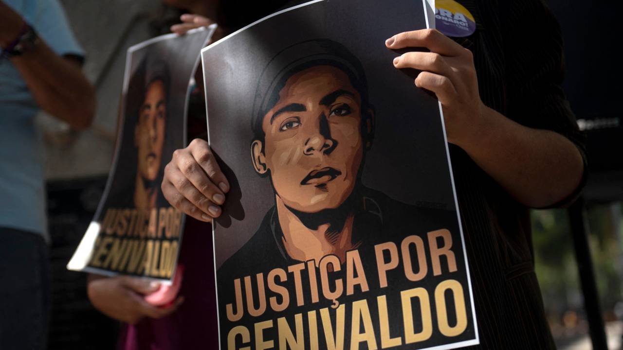 Manifestantes seguram cartazes com os dizeres “Justiça para Genivaldo” durante evento em homenagem a Genivaldo de Jesus Santos, 38 anos, no centro da cidade do Rio de Janeiro, Brasil, em 27 de maio de 2022. - Na cidade nordestina de Umbaúba, um homem morreu sufocado na quarta-feira, depois de ser colocado dentro de um porta-malas de um carro da polícia, do qual saía uma fumaça espessa. A Polícia Rodoviária Federal (PRF) disse em comunicado nesta quinta-feira que seus agentes "utilizaram técnicas de imobilização e instrumentos de baixo potencial ofensivo" ao lidar com Genivaldo de Jesus Santos, de 38 anos, que disseram ter se tornado agressivo durante uma parada de rotina . (Foto de MAURO PIMENTEL / MAURO PIMENTEL / AFP) Demonstrators hold signs reading ìJustice for Genivaldoî during an event in honor of Genivaldo de Jesus Santos, 38, at the city center of Rio de Janeiro, Brazil, on May 27, 2022. - In the northeastern town of Umbauba, a man suffocated to death on Wednesday after being placed inside a police car trunk from which thick smoke was billowing. The Federal Highway Police (PRF) said in a statement Thursday that its agents had "used immobilization techniques and instruments of low-offensive potential" in dealing with 38-year-old Genivaldo de Jesus Santos, who they said became aggressive during a routine stop. (Photo by MAURO PIMENTEL / MAURO PIMENTEL / AFP)