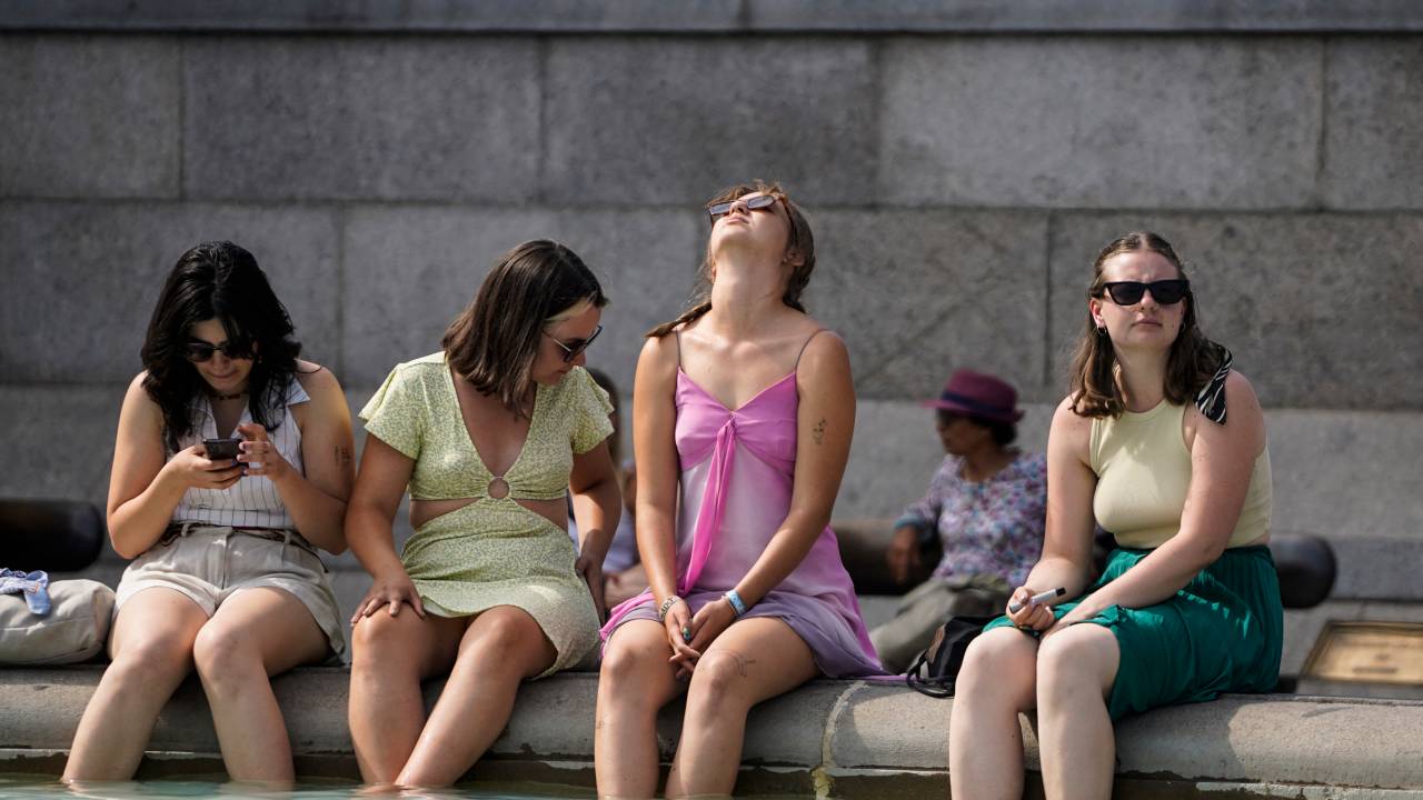 A group of women cool off by dipping their feet in the fountain of Trafalgar Square, in central London, on July 18, 2022 as the country experiences an extreme heat wave. - Britain could hit 40 Celsius (104 Fahrenheit) for the first time, forecasters said, causing havoc in a country unprepared for the onslaught of extreme heat that authorities said was putting lives at risk. (Photo by Niklas HALLE'N / AFP)