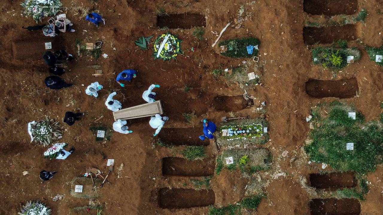 Covas de cemitério abertas, enquanto um caixão está sendo enterrado