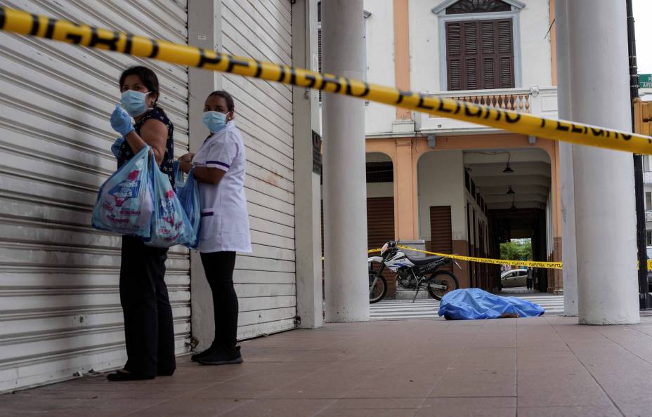 Mulheres na porta de um estabelecimento comercial, ao fundo um corpo na calçada, durante o surto da doença por coronavírus (COVID-19), em Guayaquil, Equador, em 30/03/2020.