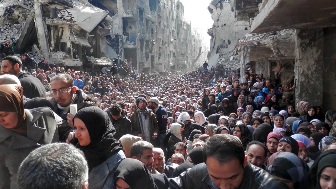 DAMASCUS, SYRIA - JANUARY 31: In this handout provided by the United Nation Relief and Works Agency (UNRWA), Residents wait in line to receive food aid distributed in the Yarmouk refugee camp on January 31, 2014 in Damascus, Syria. The United Nations renewed calls for the Syria regime and rebels to allow food and medical aid into the Palestinian camp of Yarmouk. An estimated 18,000 people are besieged inside the camp as the conflict in Syria continues. (Photo by United Nation Relief and Works Agency via Getty Images)