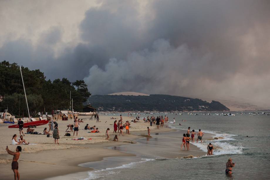 Pessoas na praia de Moulleau, ao fundo fumaça em virtude das altas temperaturas, ocasionando incêndios florestais em La Teste-de-Buch, vista de Arcachon, França, em 18/07/2022. Pessoas na praia de Moulleau, ao fundo fumaça em virtude das altas temperaturas, ocasionando incêndios florestais em La Teste-de-Buch, vista de Arcachon, França, em 18/07/2022.