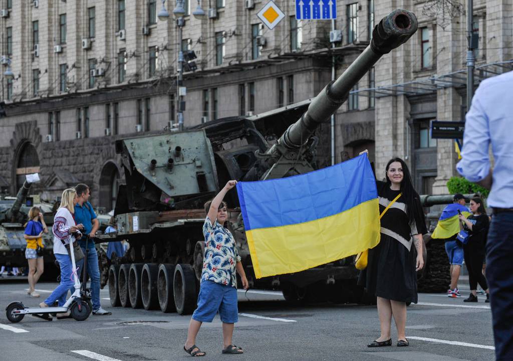 KYIV, UKRAINE - 2022/08/23: People take pictures with the Ukrainian flag near destroyed Russian army equipment displayed at Khreshchatyk in the center of Kyiv. Captured Russian military equipment is being temporarily displayed on Khreschaytk street in the heart of the Ukrainian capital. The area has become a popular attraction among residents curious to see Ukraine's spoils of war. (Photo by Sergei Chuzavkov/SOPA Images/LightRocket via Getty Images)
