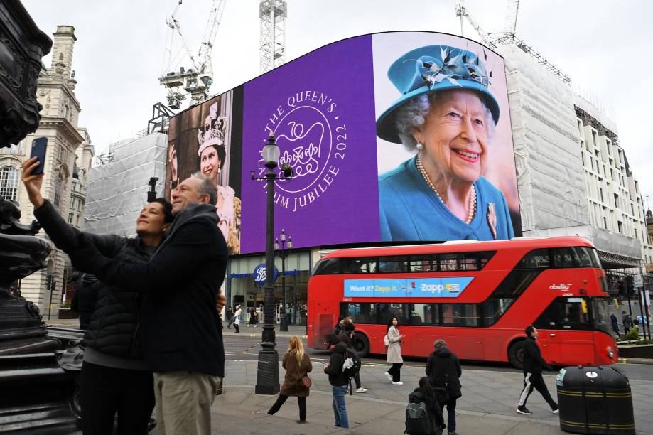 Um casal tira uma selfie enquanto as imagens da rainha Elizabeth II da Grã-Bretanha são exibidas -