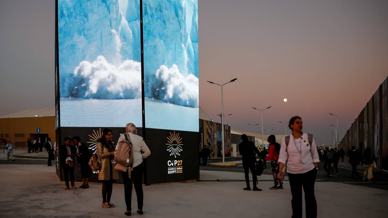 Participantes caminham em frente a uma tela com o logotipo da COP27 no segundo dia da Conferência das Nações Unidas sobre Mudanças Climáticas COP27, realizada pela UNFCCC no Centro Internacional de Convenções de Sharm El-Sheikh, Egito, em 7 de novembro de 2022. COP27, de 6 a novembro 18 em Sharm El Sheikh concentra-se na implementação de medidas já acordadas em COPs anteriores. A Conferência em Sharm El Sheikh também se concentra nas comunidades mais vulneráveis, pois a crise climática endurece as condições de vida das pessoas já mais desfavorecidas.