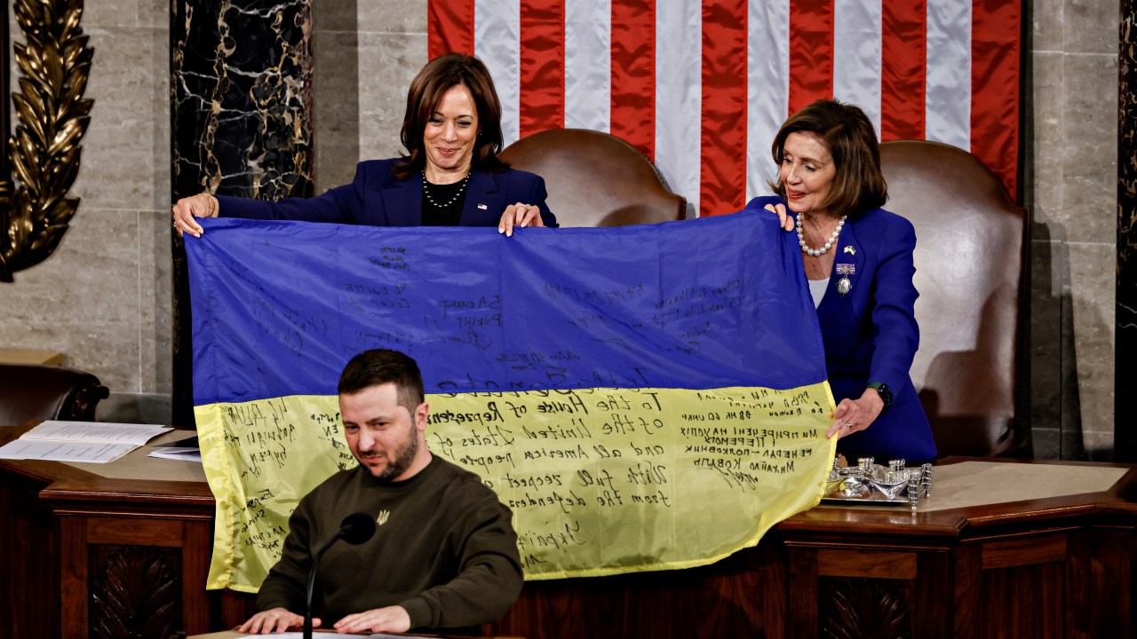 A presidente da Câmara dos EUA, Nancy Pelosi, à direita, e a vice-presidente dos EUA, Kamala Harris, à esquerda, seguram uma bandeira ucraniana assinada por soldados em Bakhmutto devastada pela guerra após ser apresentada por Volodymyr Zelenskiy, presidente da Ucrânia, em baixo, durante uma reunião conjunta do Congresso no Capitólio dos EUA em Washington. 21/12/2022