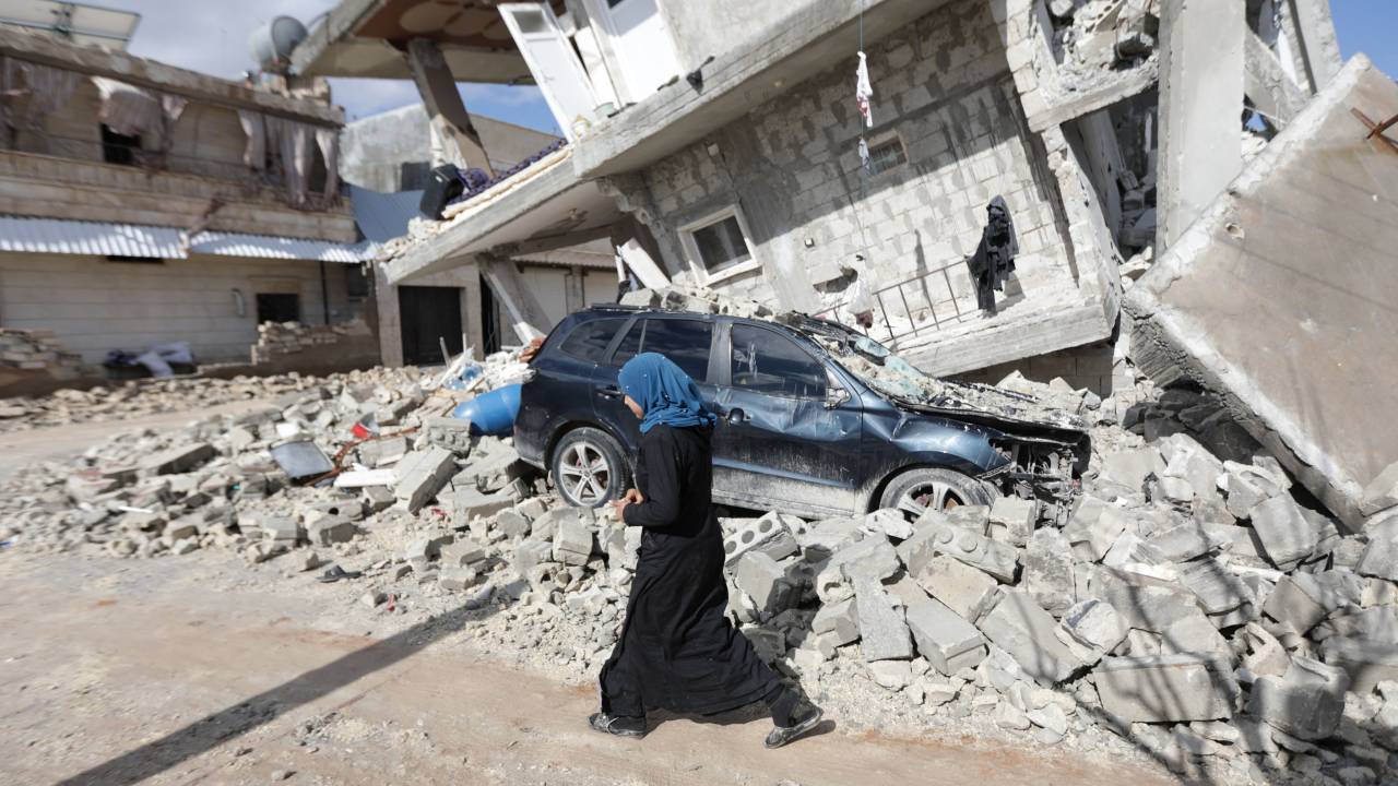 A Syrian woman walks past a half collapsed house in the town of Azaz on the border with Turkey on February 7, 2023, following a deadly earthquake. - The Syrian Red Crescent appealed to Western countries to lift sanctions and provide aid after a powerful earthquake has killed more than 1,600 people across the war-torn country. The 7.8-magnitude quake early the previous day, which has also killed thousands in neighbouring Turkey, led to widespread destruction in both regime-controlled and rebel-held parts of Syria. (Photo by Bakr ALKASEM / AFP)